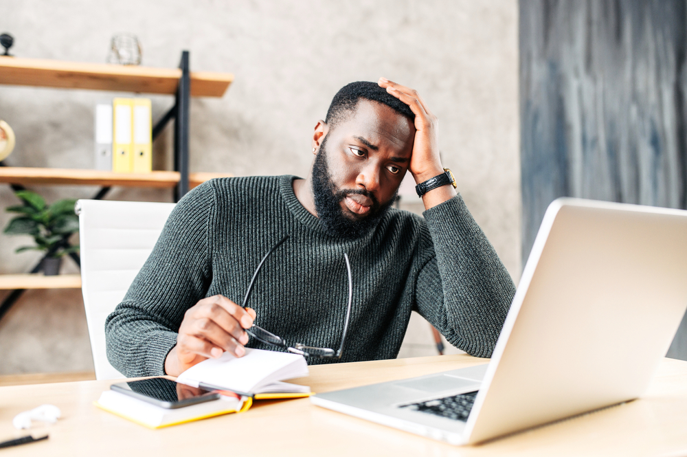 A frustrated, sad man looks at his computer and worries about his debts and weighs his options to get out of debt