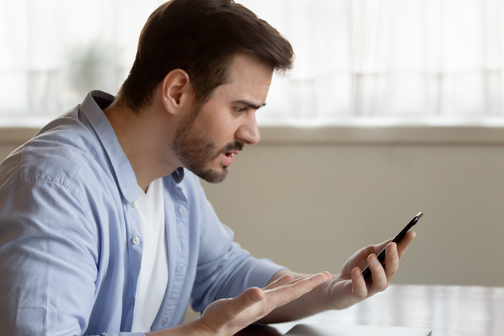 A man with an angry expression looks at his cell phone