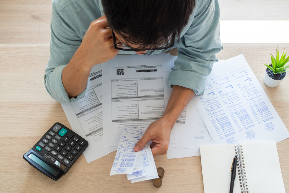 A man is seen from overhead looking at all his bills and trying to figure out how to pay them off as he considers debt consolidation