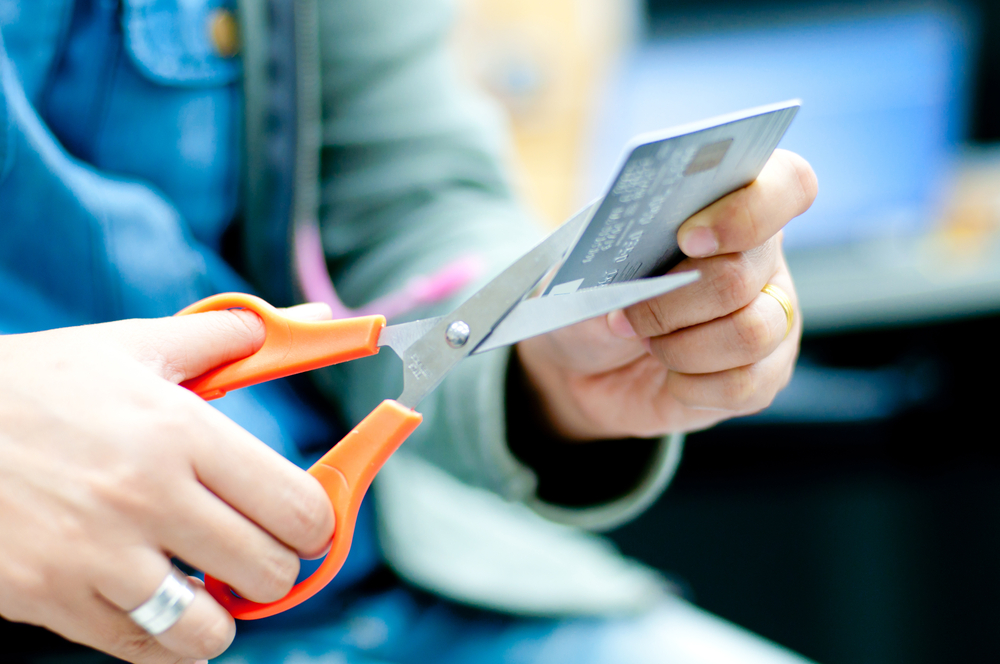 A closeup of hands are shown, using scissors to cut up a credit card