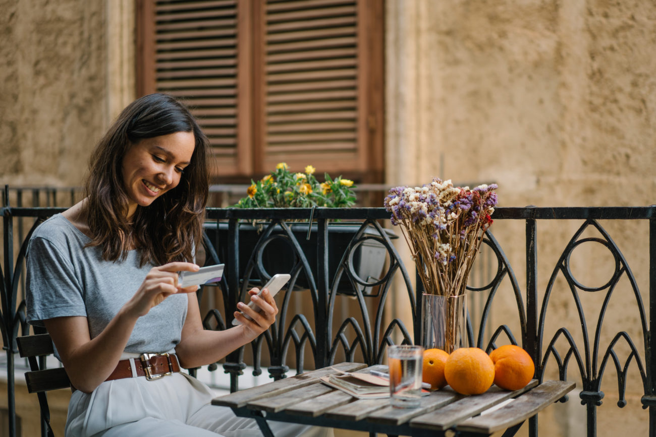 A woman holds her credit card while sitting on a balcony