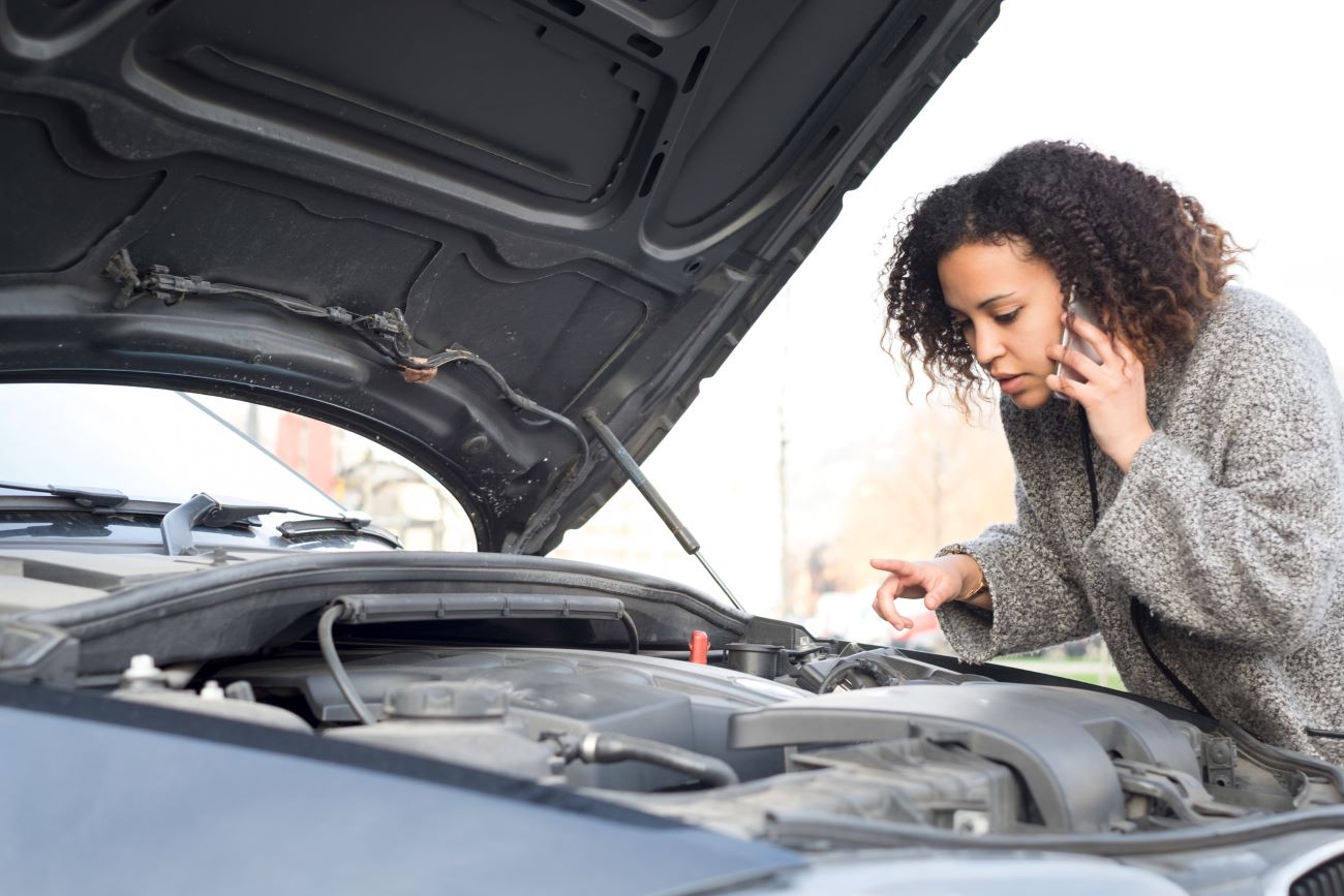 a woman looks under the hood of her car and will need money to get her car fixed