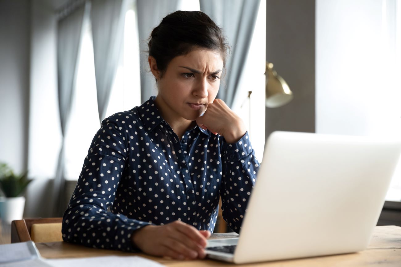 A woman is upset as she looks at her computer and sees that her identity has been stolen