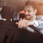 a man uses his savings to buy a new car and looks happy behind the wheel