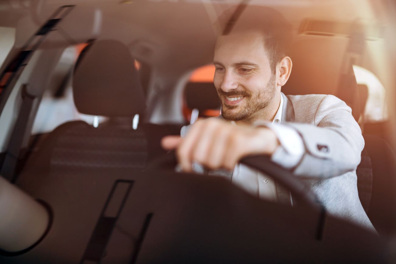a man uses his savings to buy a new car and looks happy behind the wheel