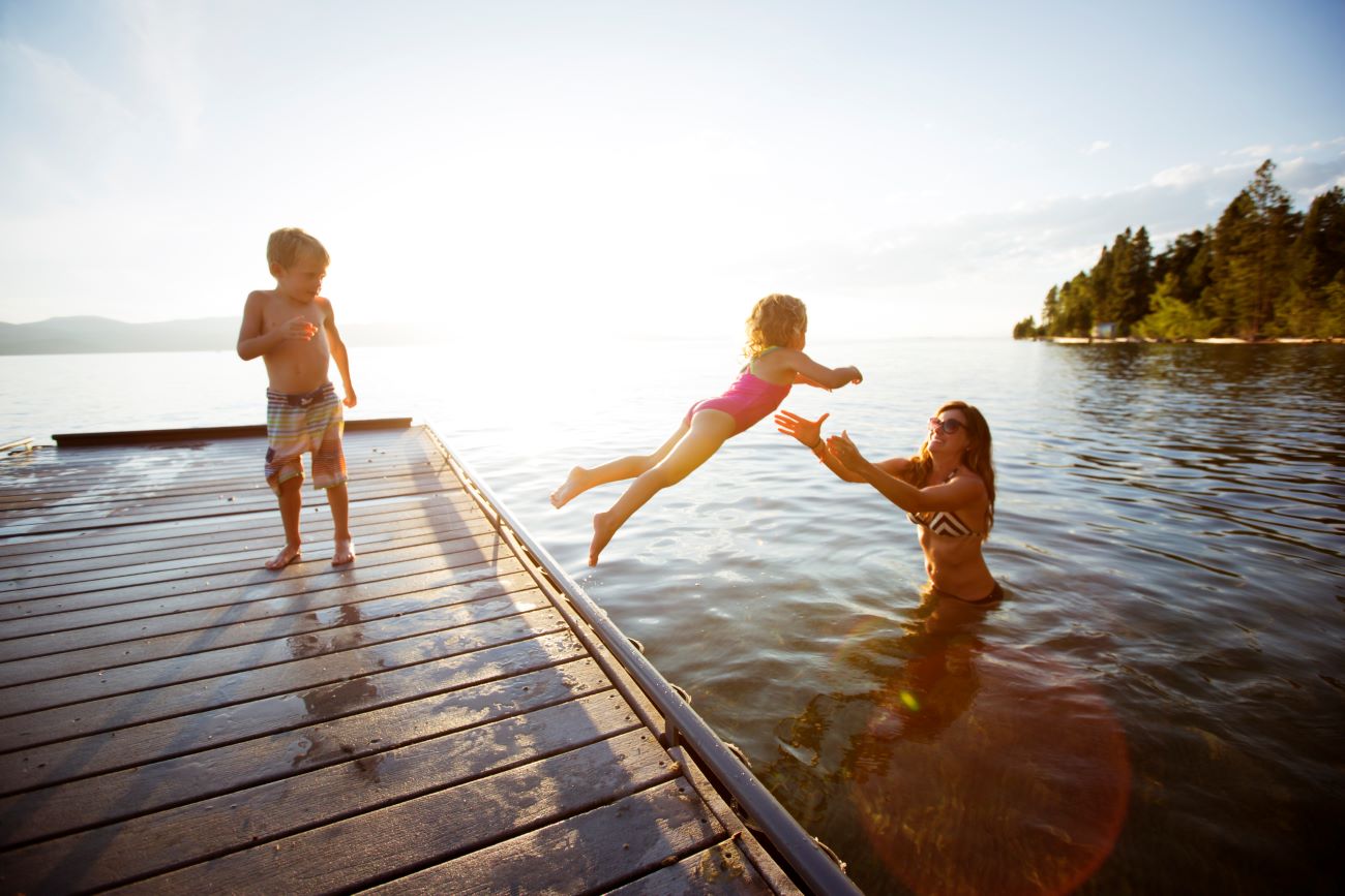A family enjoys a summer day at the lake. A child jumps off a platform into her mother's arms, while another child looks on