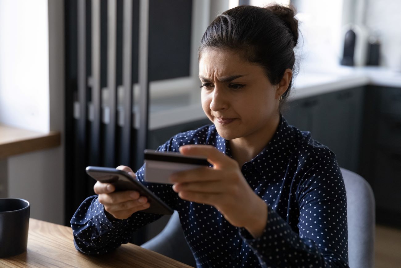 A woman looks at her phone and credit card as she deals with credit card fraud