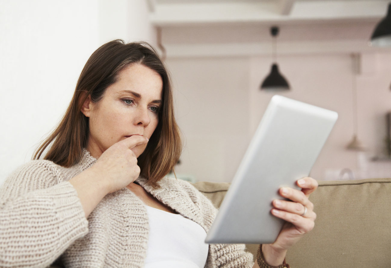 A woman wears a serious expression while looking for a legitimate personal loan on her computer tablet