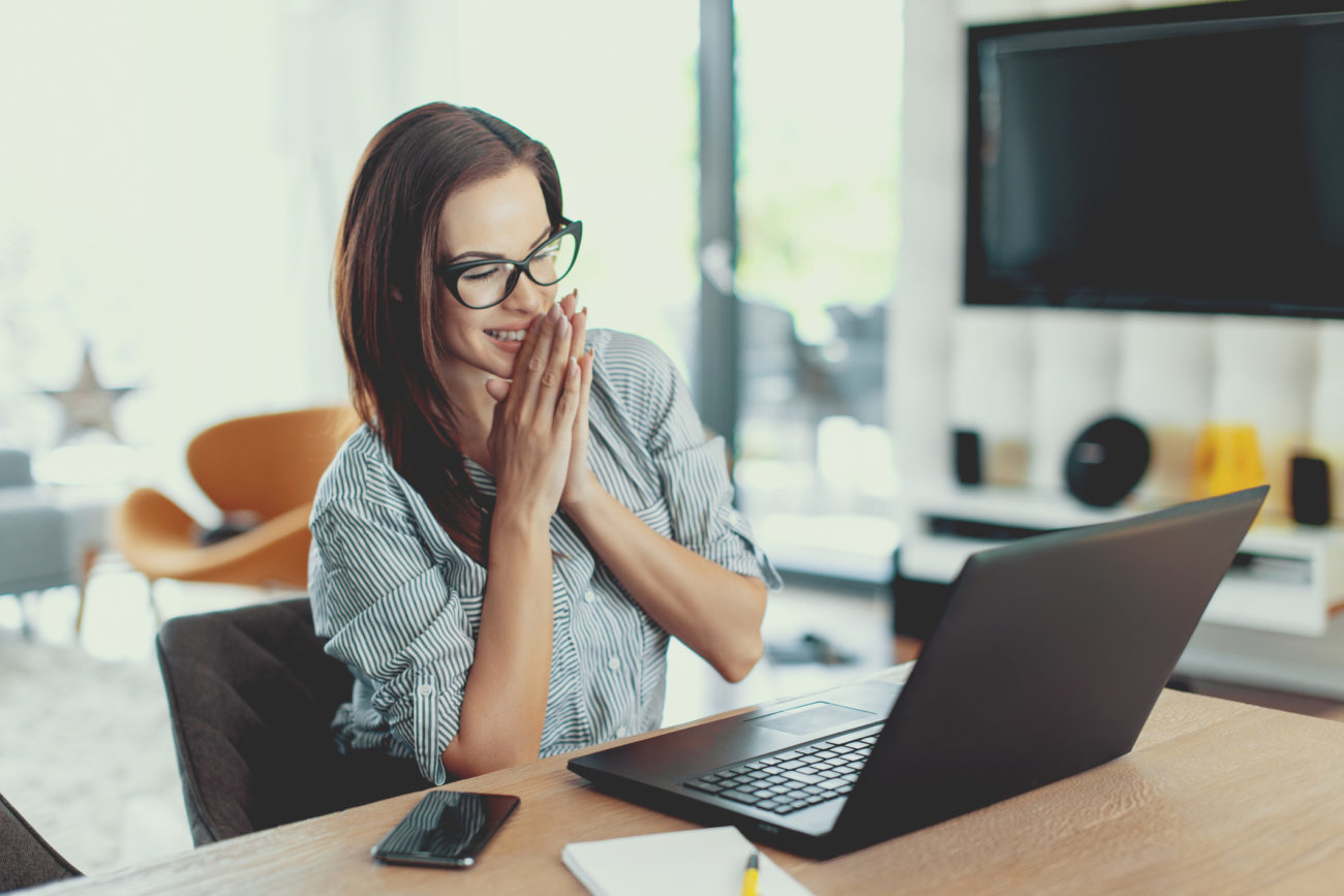 A woman looks at her computer with a happy expression because she is approved for a personal loan