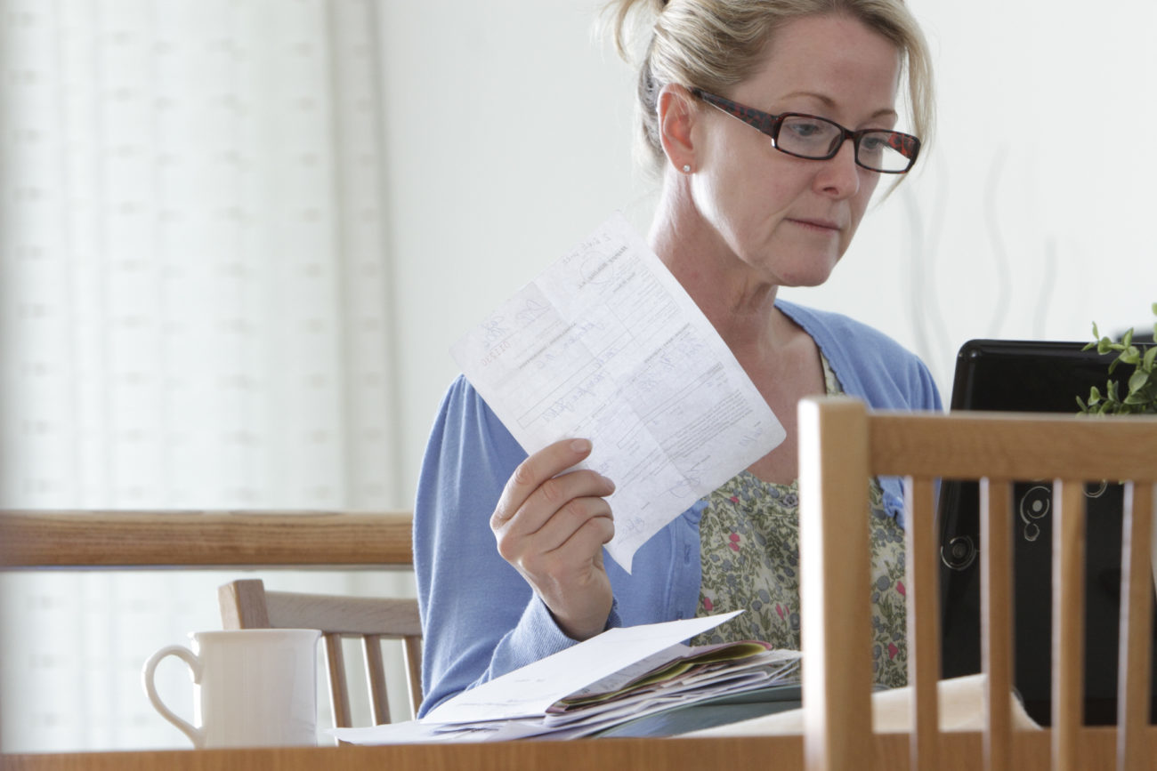 A woman sits in front of a computer holding a bill and considers paying her personal loan off early.