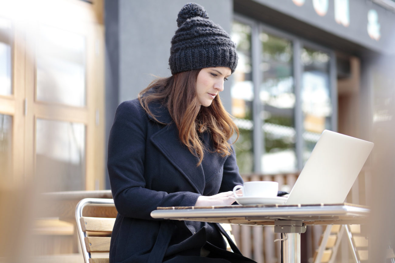 A young woman applies for a personal loan using her computer while sitting at a cafe.