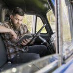A man sits inside of his truck while looking at his computer tablet to apply for a personal loan.