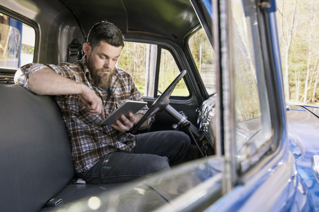 A man sits inside of his truck while looking at his computer tablet to apply for a personal loan.