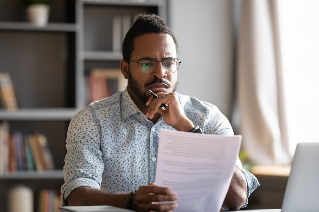 A man has a concerned look on his face while reading a letter as he sits at his desk