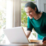 A woman looks at her credit score on her laptop computer with a smile on her face