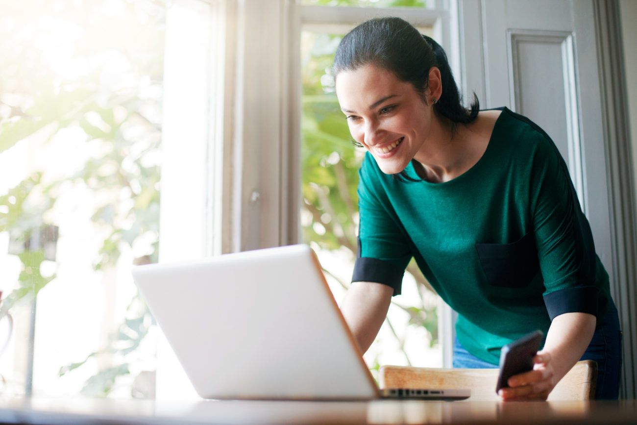 A woman looks at her credit score on her laptop computer with a smile on her face