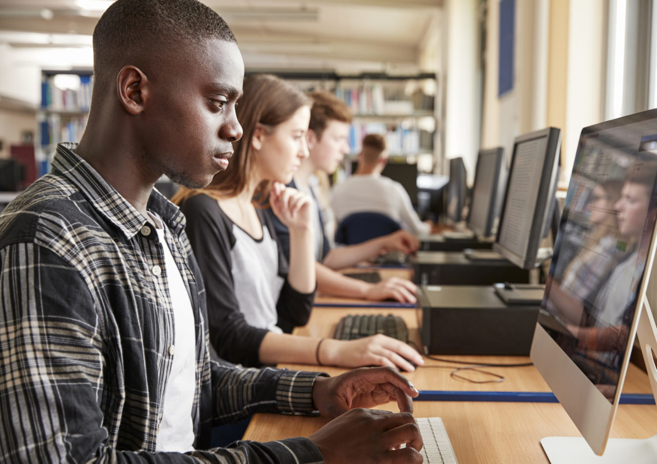 College students sit at a long table in the library while working on their computers