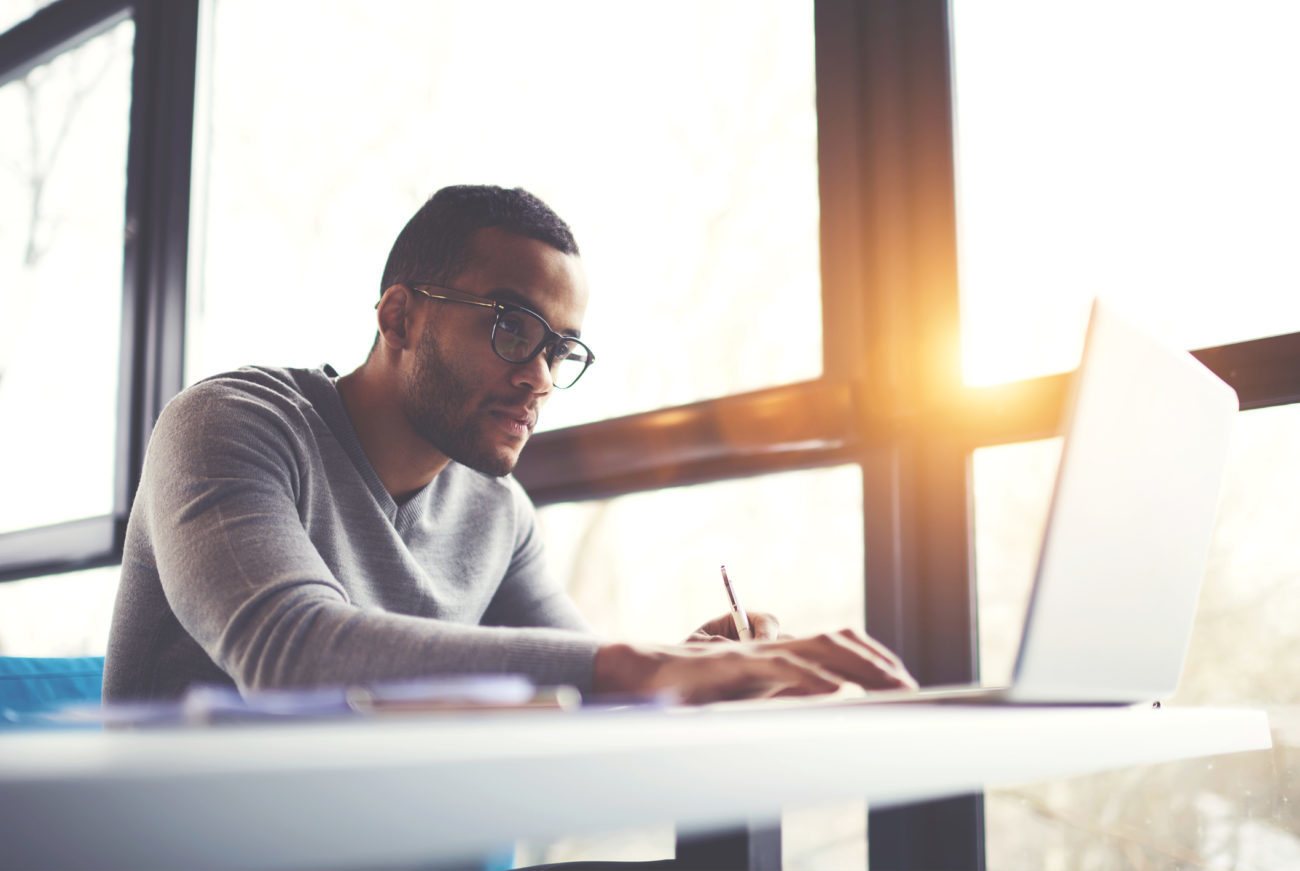 A man sits at his computer and takes notes as he applies for a personal loan online