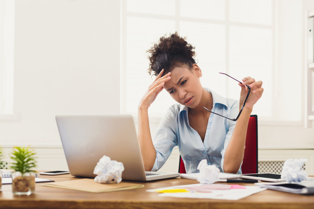 A woman sits at her computer and rubs her temple while she considers debt management help