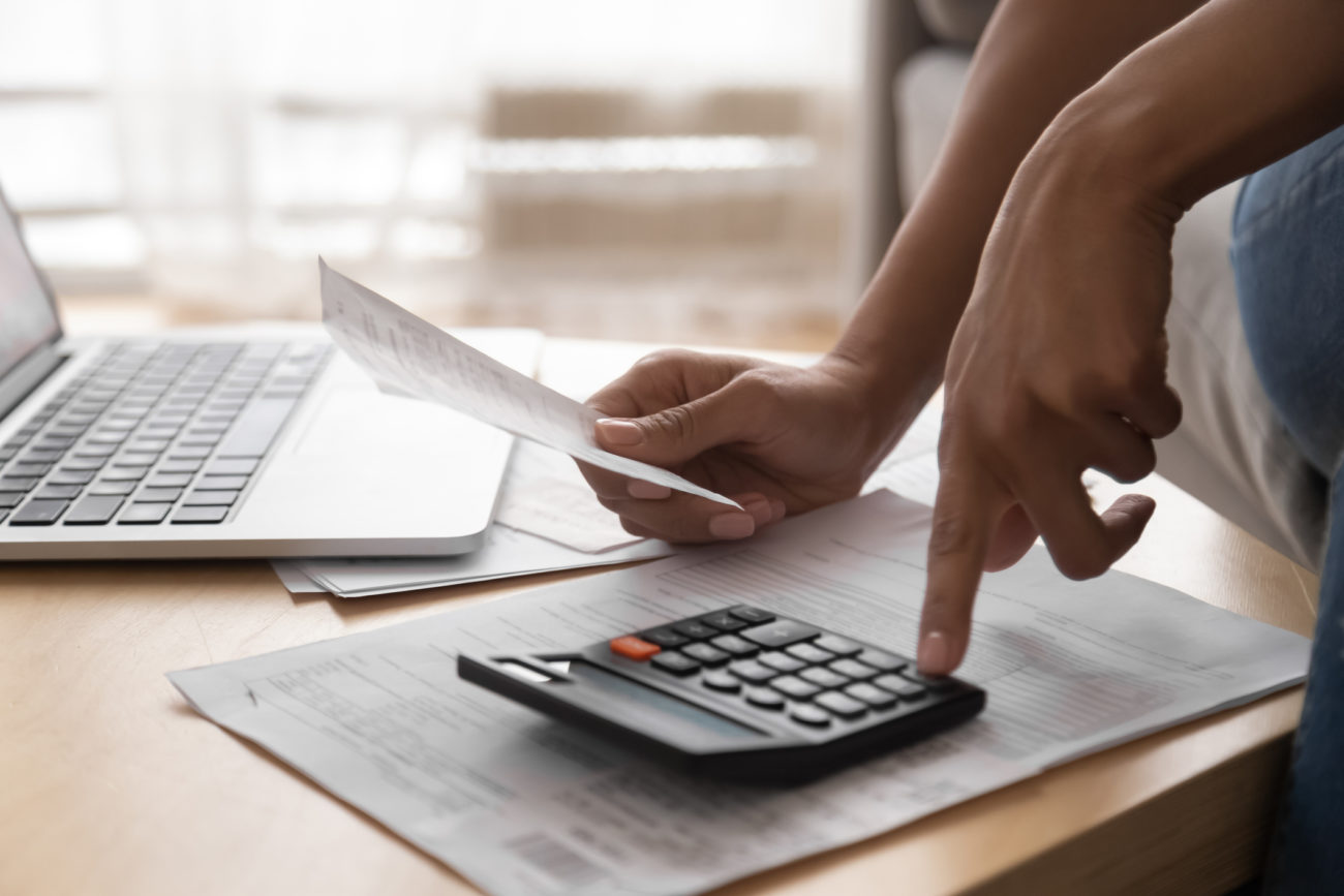 A woman works on her finances using a calculator and holding a bill.