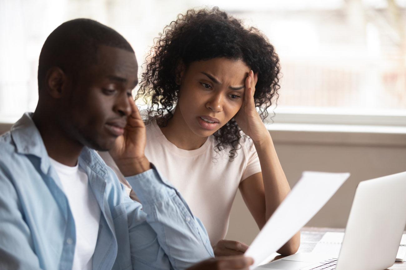 A stressed out couple sits at their computer and discusses their debts.