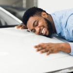 A man smiles as he hugs his new car after getting an auto loan