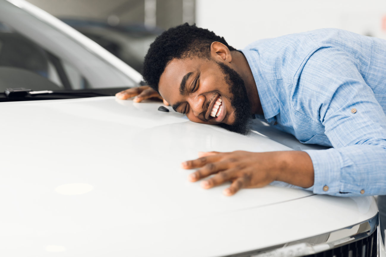 A man smiles as he hugs his new car after getting an auto loan