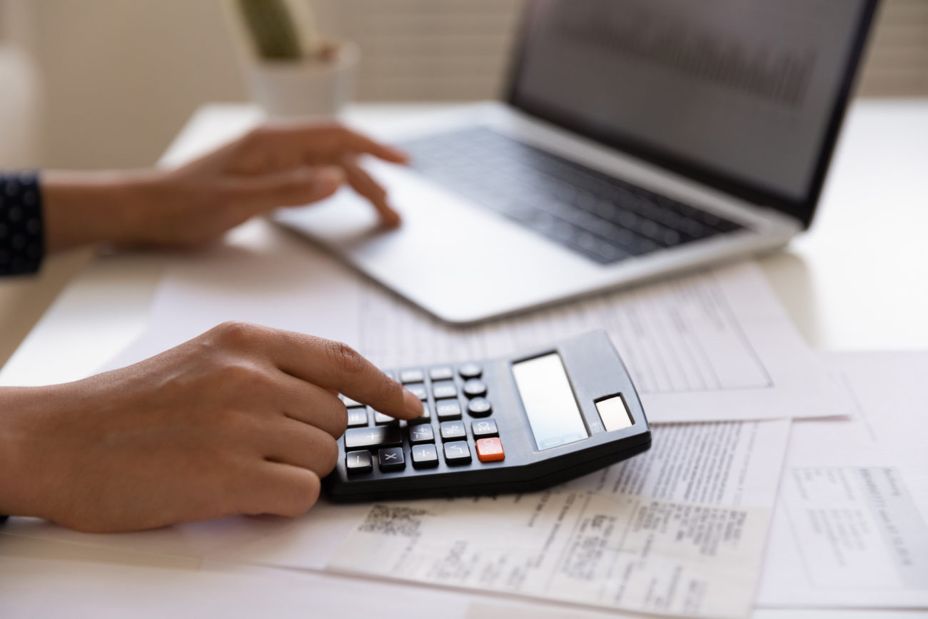 closeup of a woman's hands using her computer and a calculator to compute credit utilization