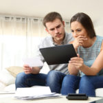 A man and woman with worried expressions check their finances using their computer