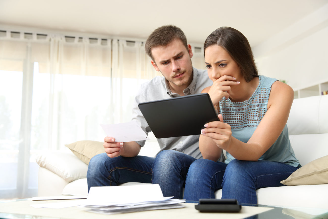 A man and woman with worried expressions check their finances using their computer