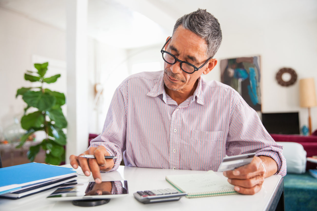 A man holds a credit card and uses his cell phone to make an online purchase