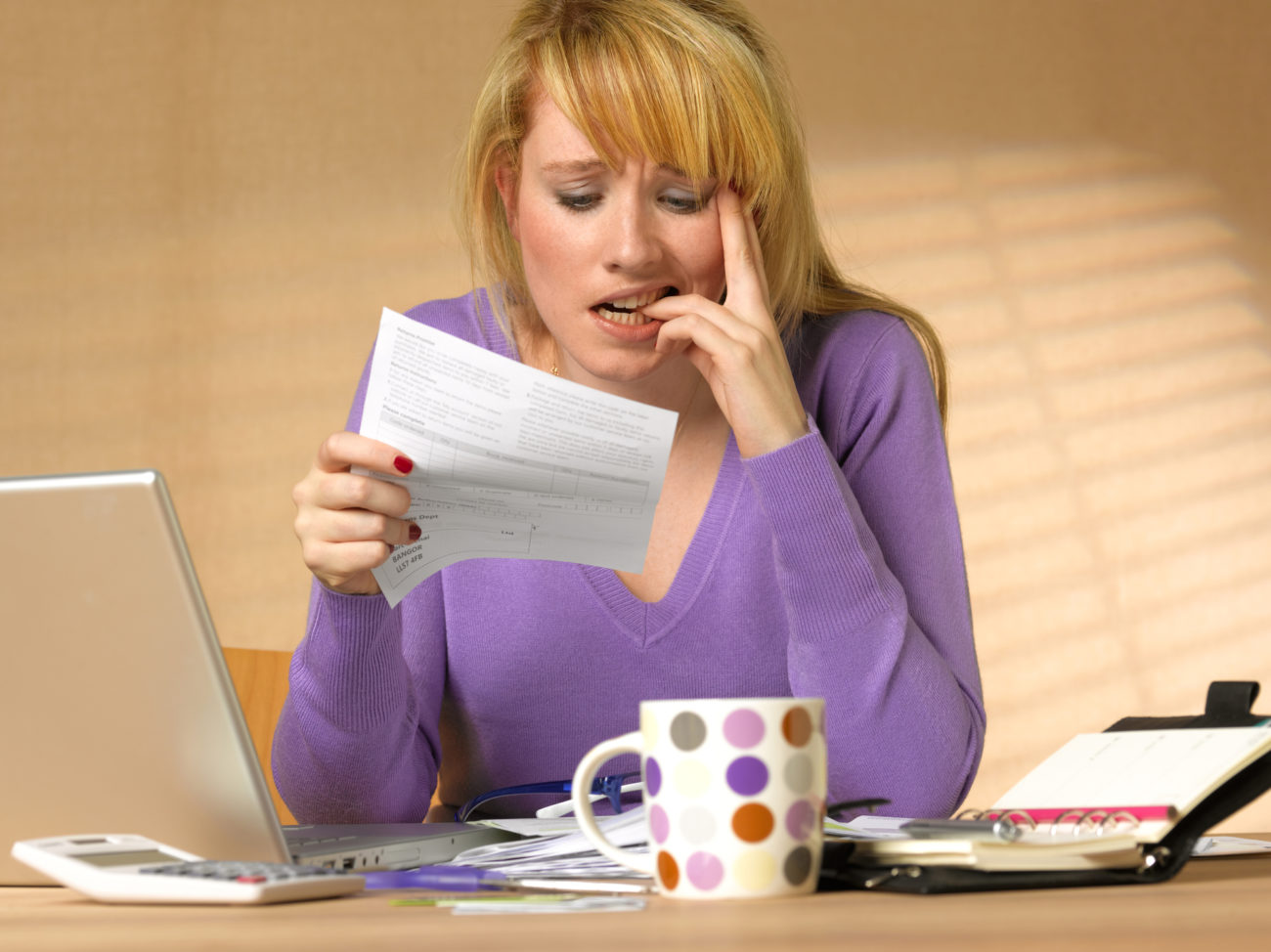 A stressed out woman is sitting in front of her computer and looking at a bill while she tries debt management