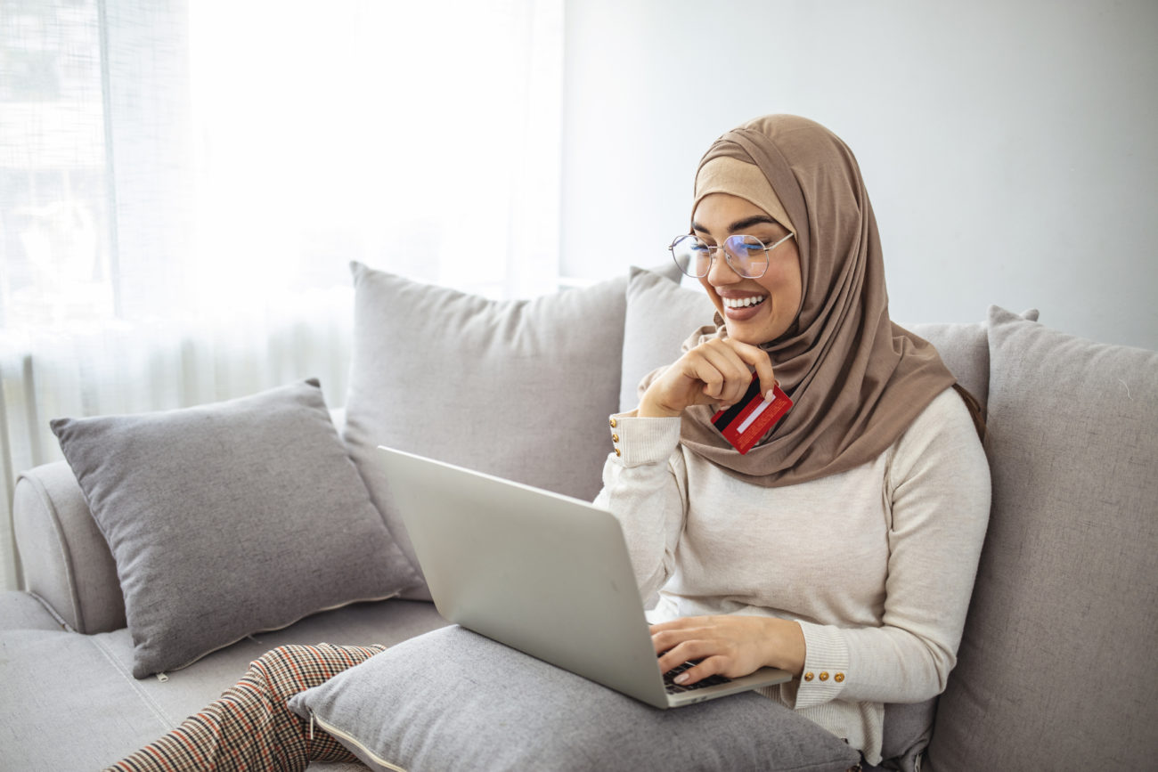 A woman holds a credit card while using her laptop to shop online