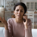 A woman with a worried expression talks to a debt collector on the phone