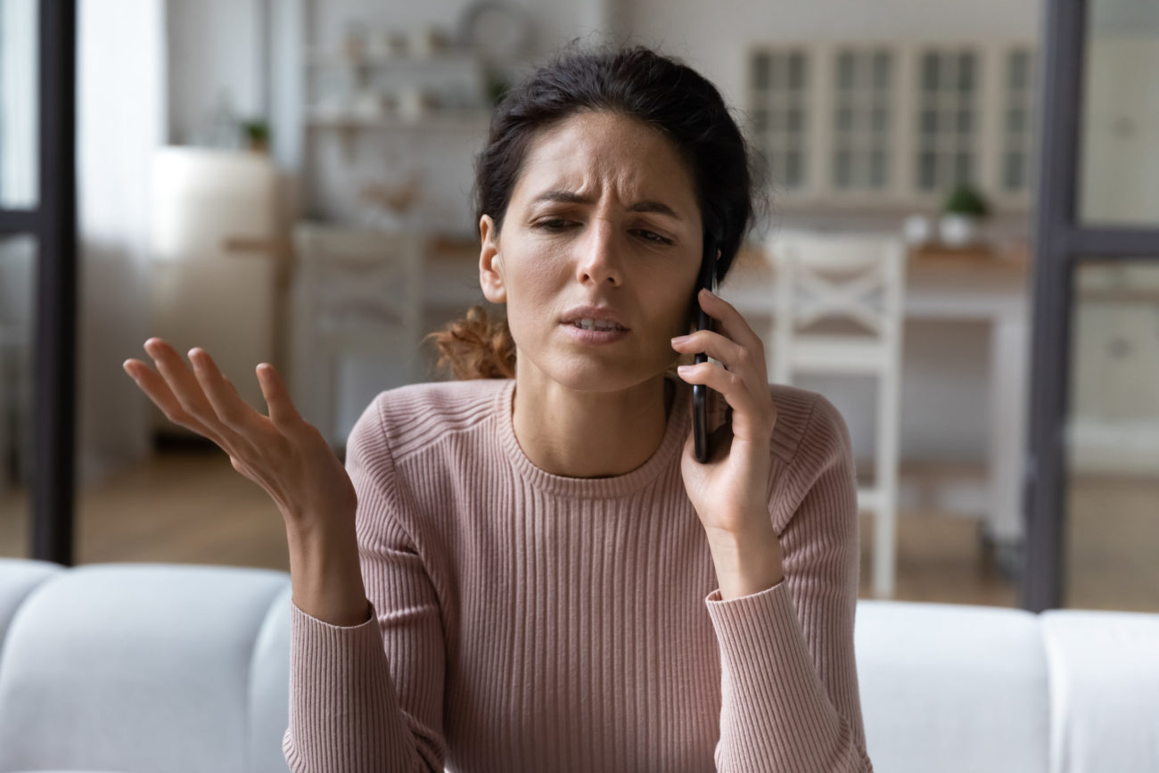 A woman with a worried expression talks to a debt collector on the phone
