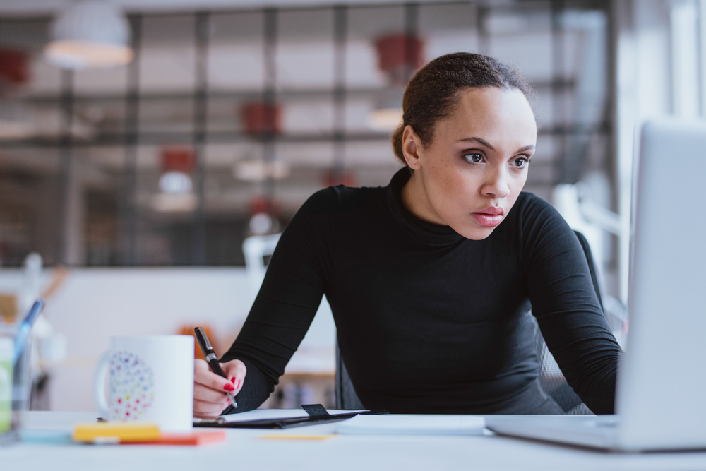 A young woman stares intently at a computer while taking notes