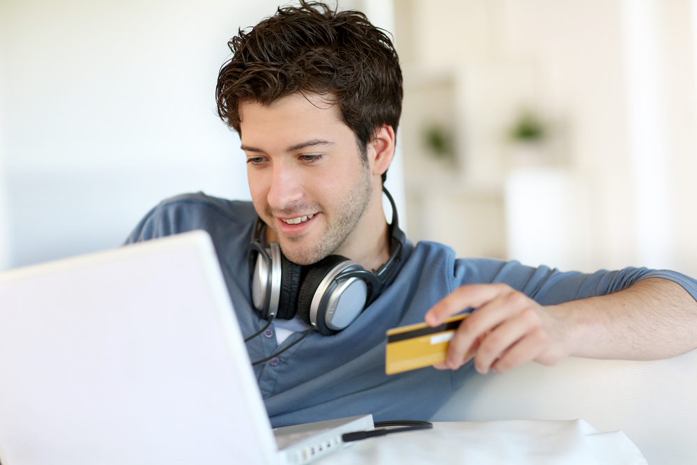 A young man holds a credit card while looking at his computer as he learns how to use credit responsibly