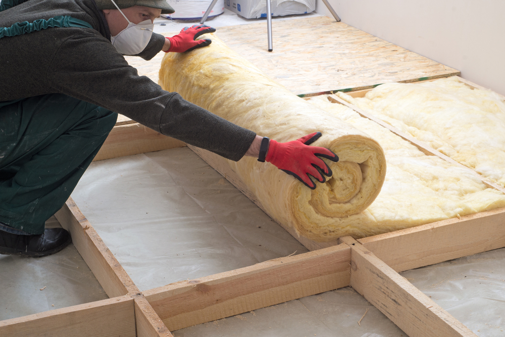 A home improvement professional wearing protective equipment installs installation into an attic