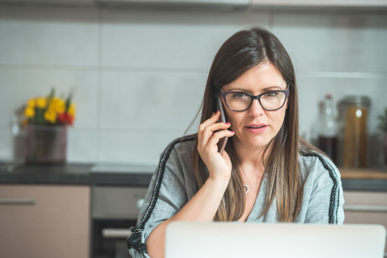 a woman talks on her phone while looking at her computer with a serious expression