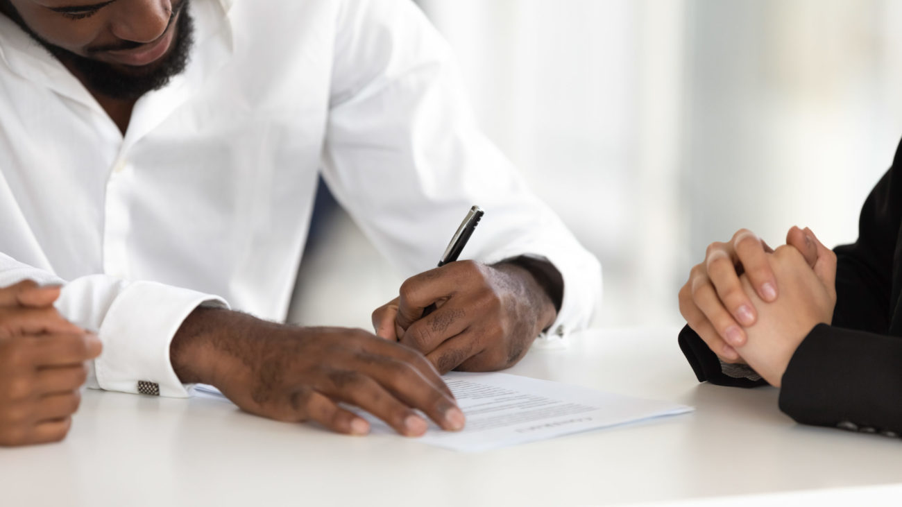 A man signs documents for a personal loan while the loan officer watches