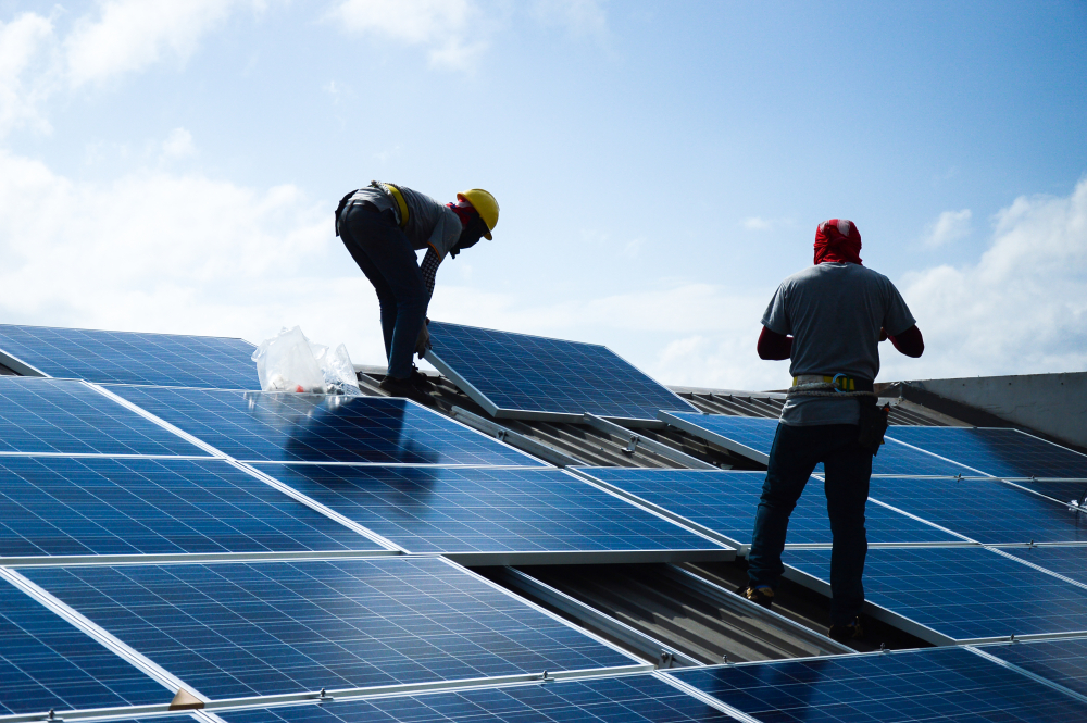 Two workers are seen installing solar panels on a building