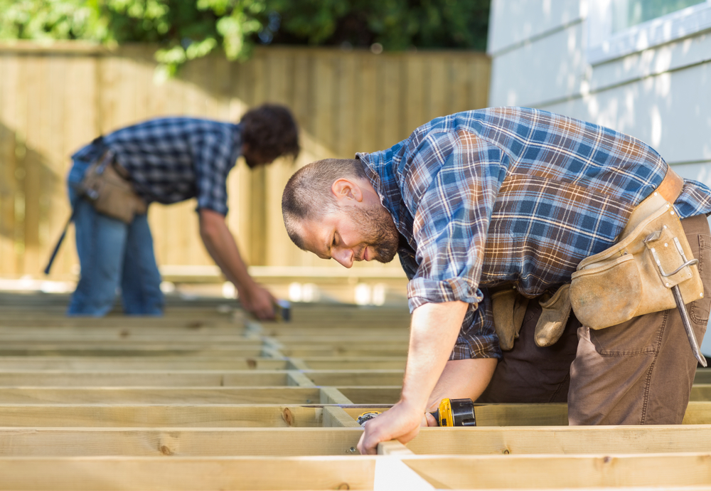 Two home improvement contractors are shown building a deck outdoors