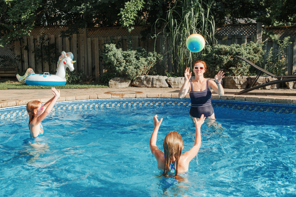 A family enjoys their backyard pool as they throw a beach ball around in the water