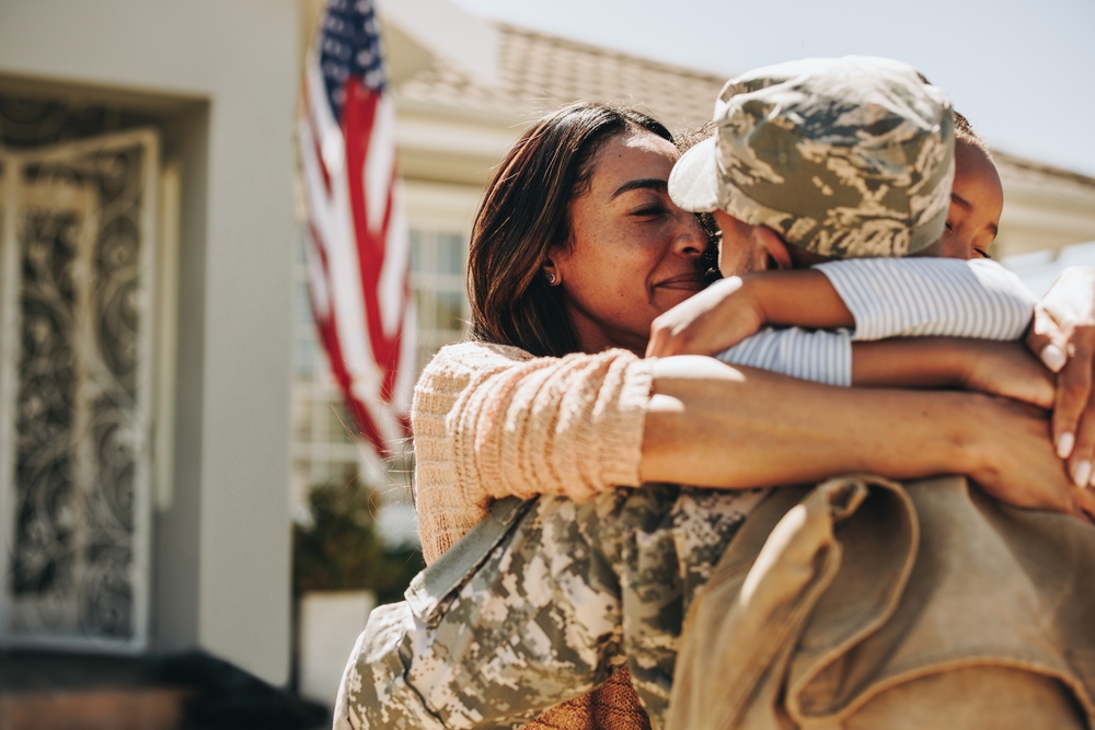 A military member arrives home to a hug from his wife and child