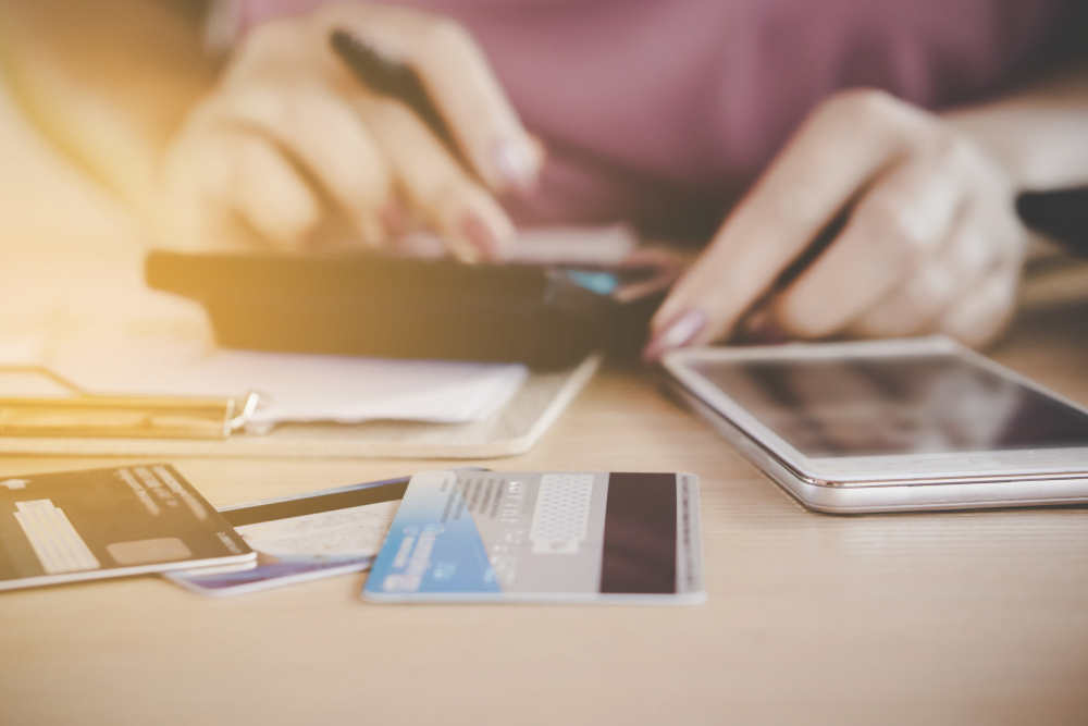 A woman's hands can be seen using a calculator to determine her debts while a pile of credit cards sits next to her